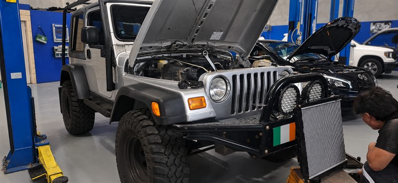 Silver Jeep Wrangler TJ with the bonnet up and a mechanic at work