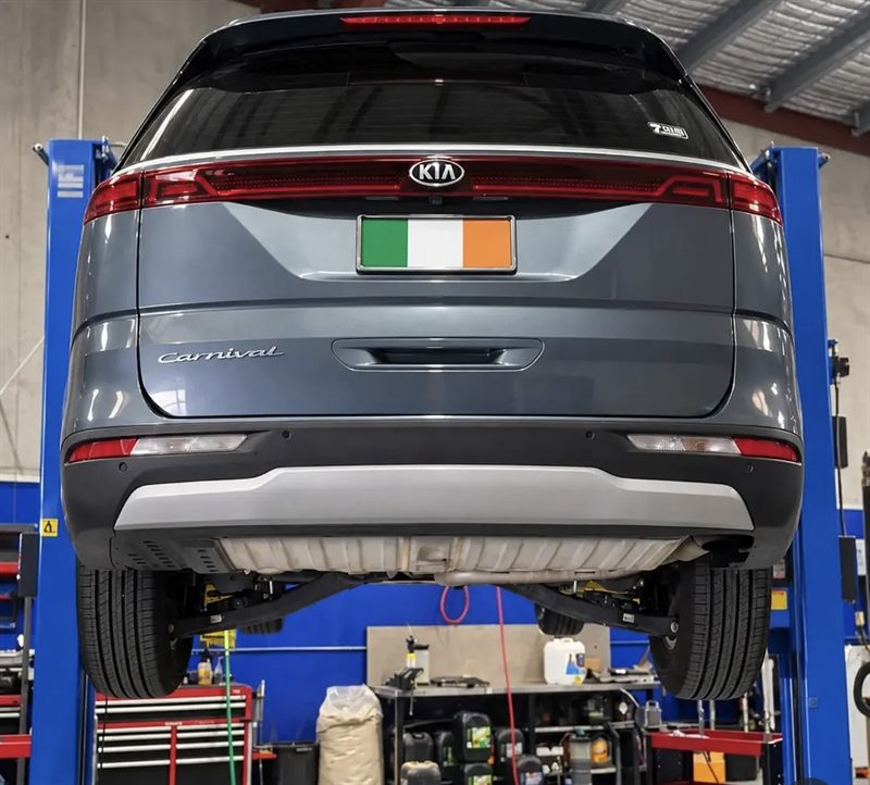 Grey Kia Carnival raised on a two-post hoist, seen from the rear