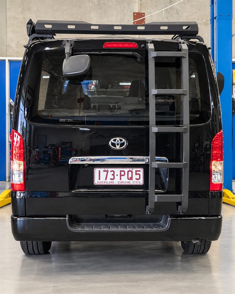 Rear of a black Toyota HiAce camper with ladder and roof rack
