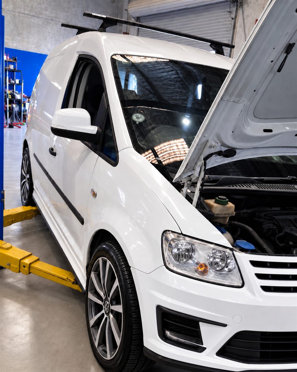 White Volkswagen Caddy with the bonnet up on hoist arms