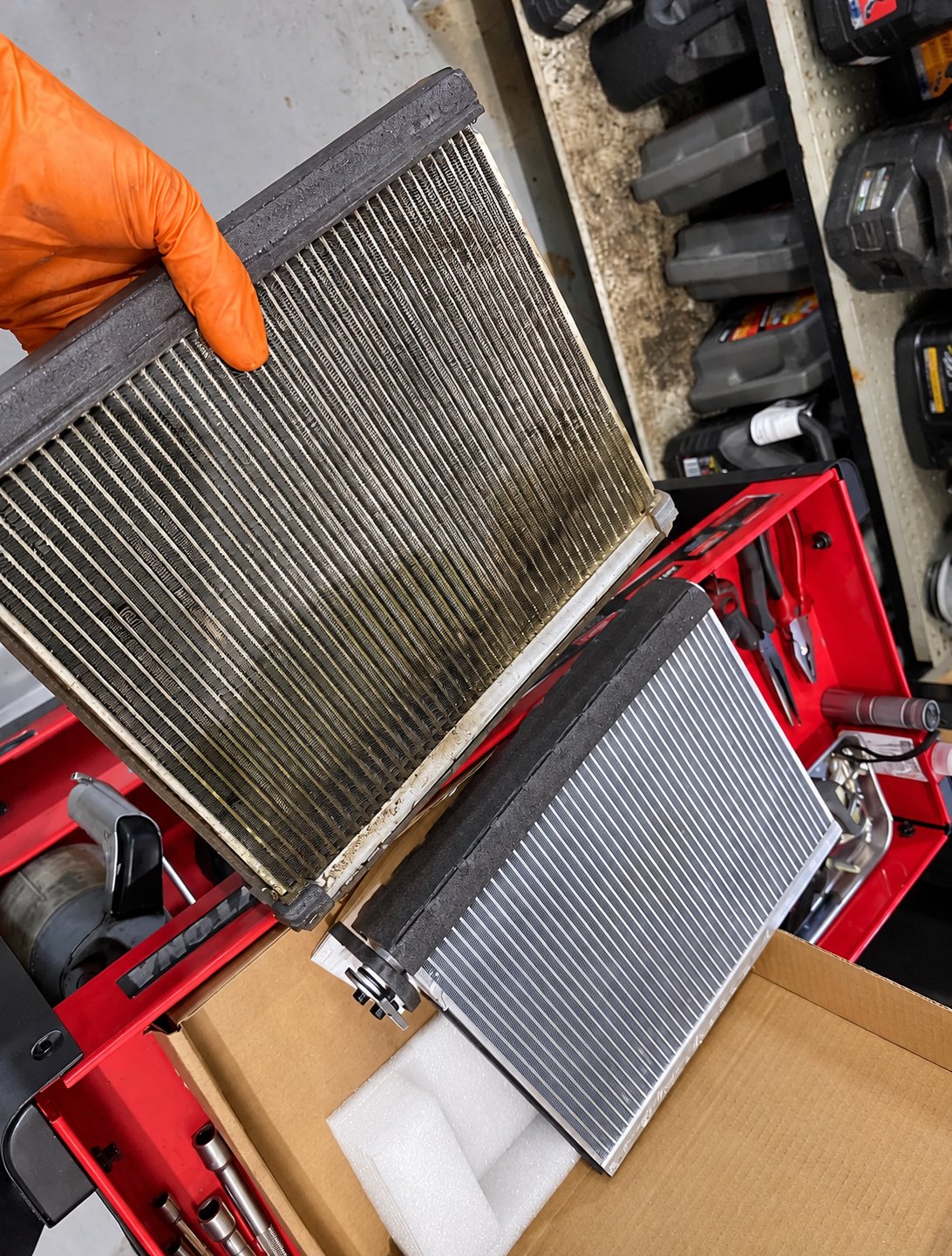 Old clogged cabin filter held next to a new air-conditioning condenser