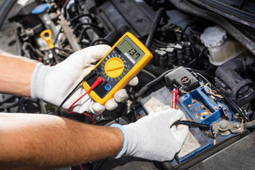 A person in gloves uses a multimeter to check a battery, highlighting the link between engine diagnostics and fuel efficiency.